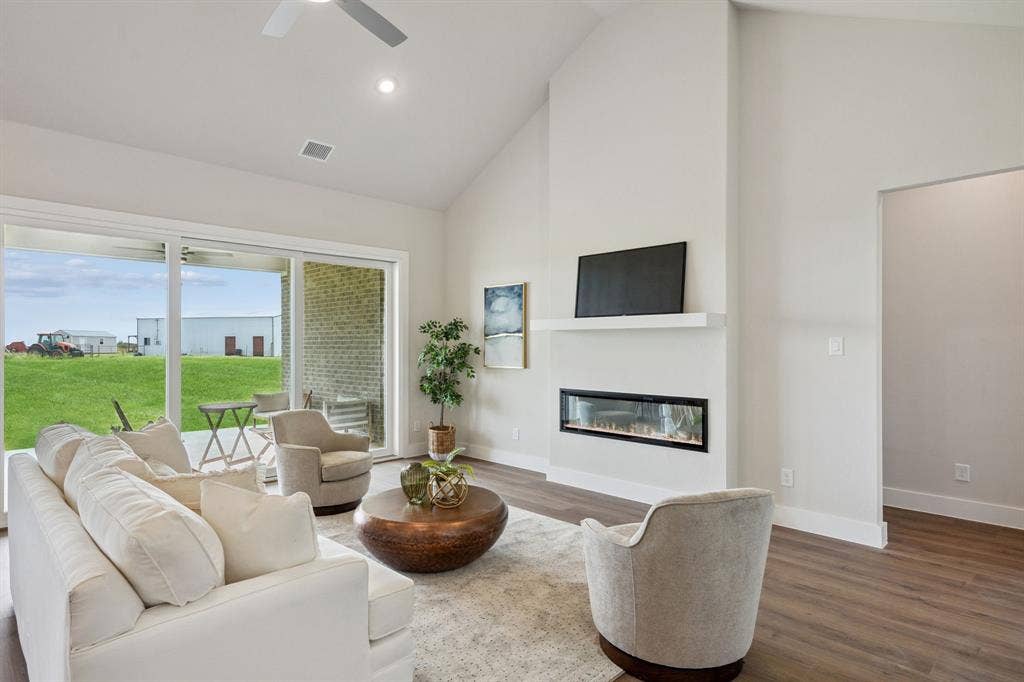 151 Quiet Waters Way, Waxahachie, TX 75165 Modern living room featuring a linear fireplace with integrated media niche, wood-finish flooring, and expansive glass doors opening to a manicured lawn