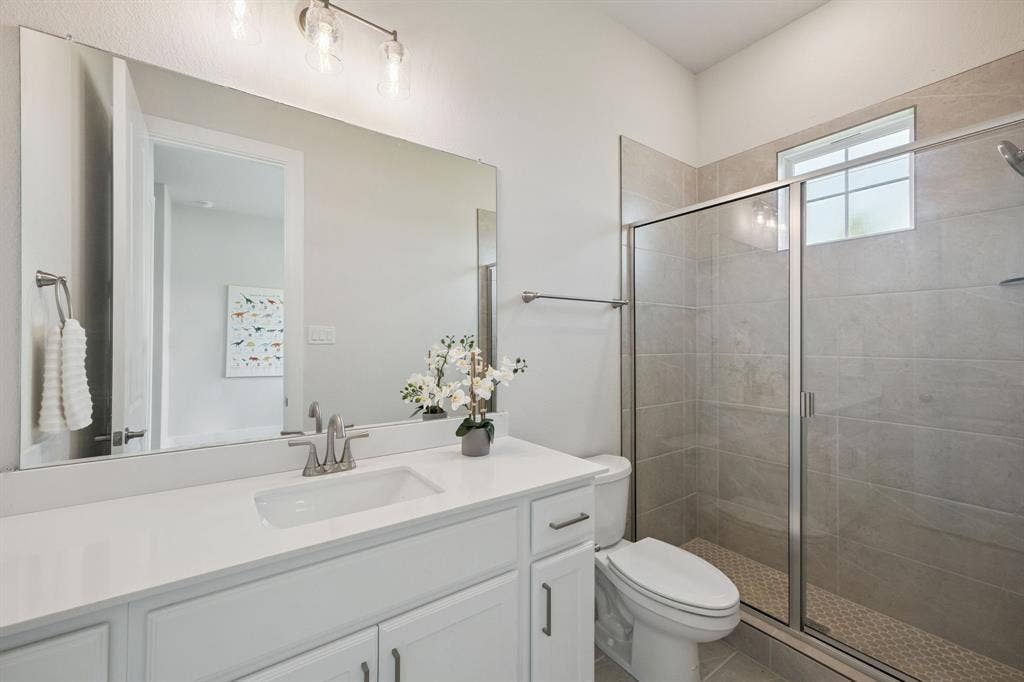 151 Quiet Waters Way, Waxahachie, TX 75165 Bathroom featuring a white vanity with a light-toned countertop, large wall-mounted mirror, three-light fixture, and a glass-enclosed shower with tile surround