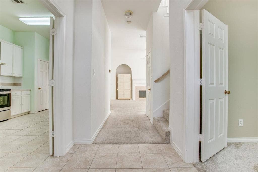 Interior entryway featuring tile flooring, six-panel interior doors, carpeted staircase, and an arched architectural opening