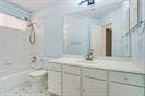 Bathroom featuring a white vanity cabinet, solid-surface countertop with an integrated sink, large wall-mounted mirror, and a tub-shower combination with a chrome showerhead