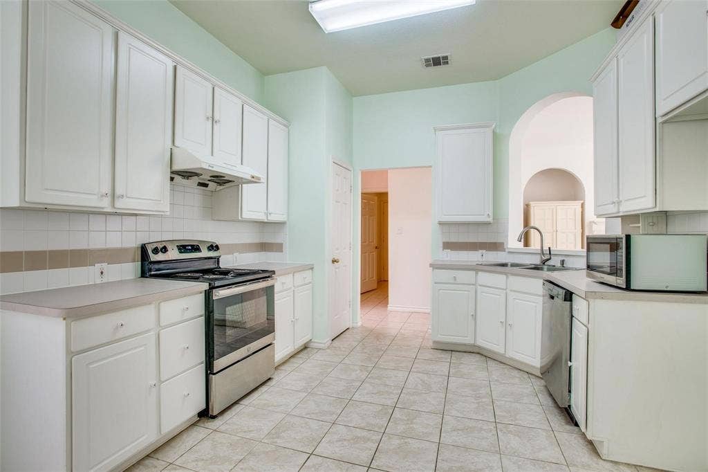 Kitchen featuring white cabinetry, stainless steel oven, tile flooring, ceramic tile backsplash, and a pass-through arched opening
