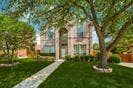 Two-story brick exterior featuring a multi-gabled roofline, arched entryway, stone-paved walkway, and mature landscaping