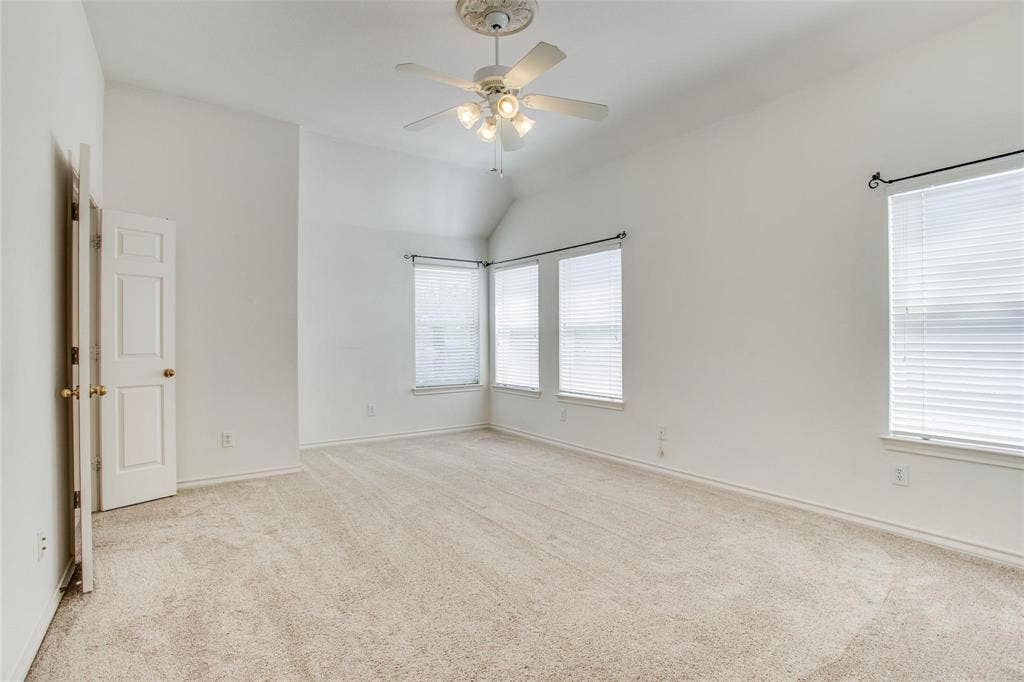 Vaulted ceilings with a decorative ceiling medallion, integrated multi-blade ceiling fan, neutral wall-to-wall carpeting, and multiple windows with horizontal blinds