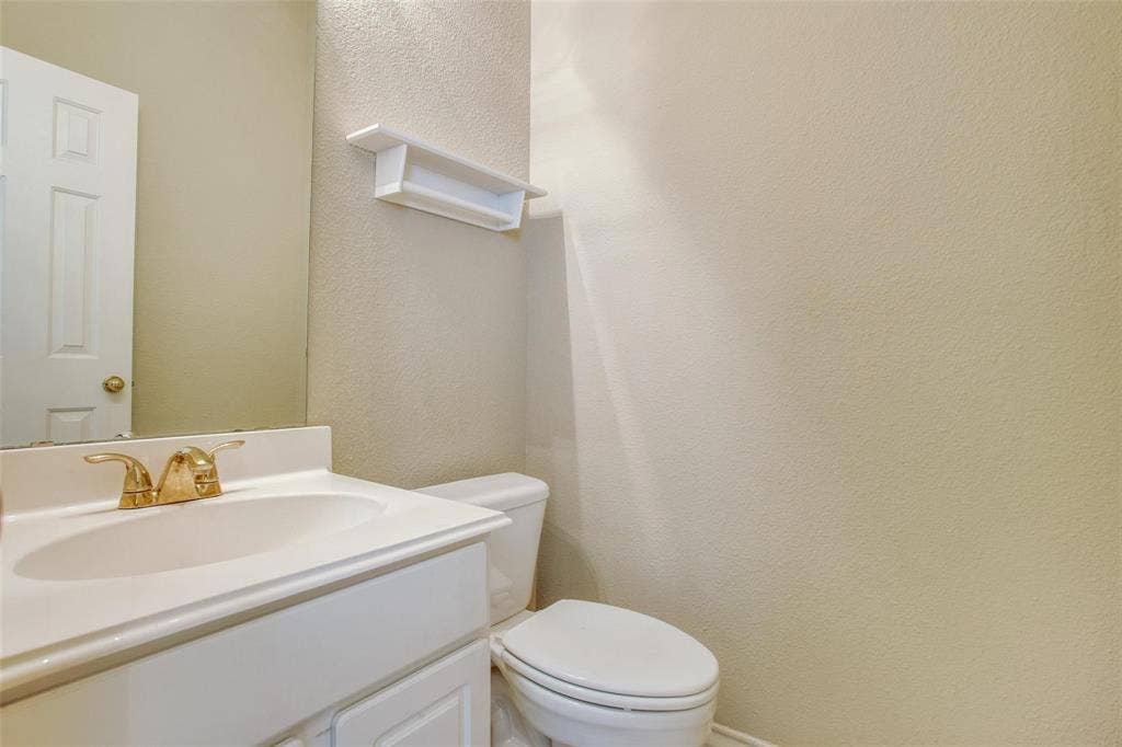 Single-sink vanity with a solid-surface countertop, gold-tone faucet, wall-mounted storage shelf, and neutral wall finish
