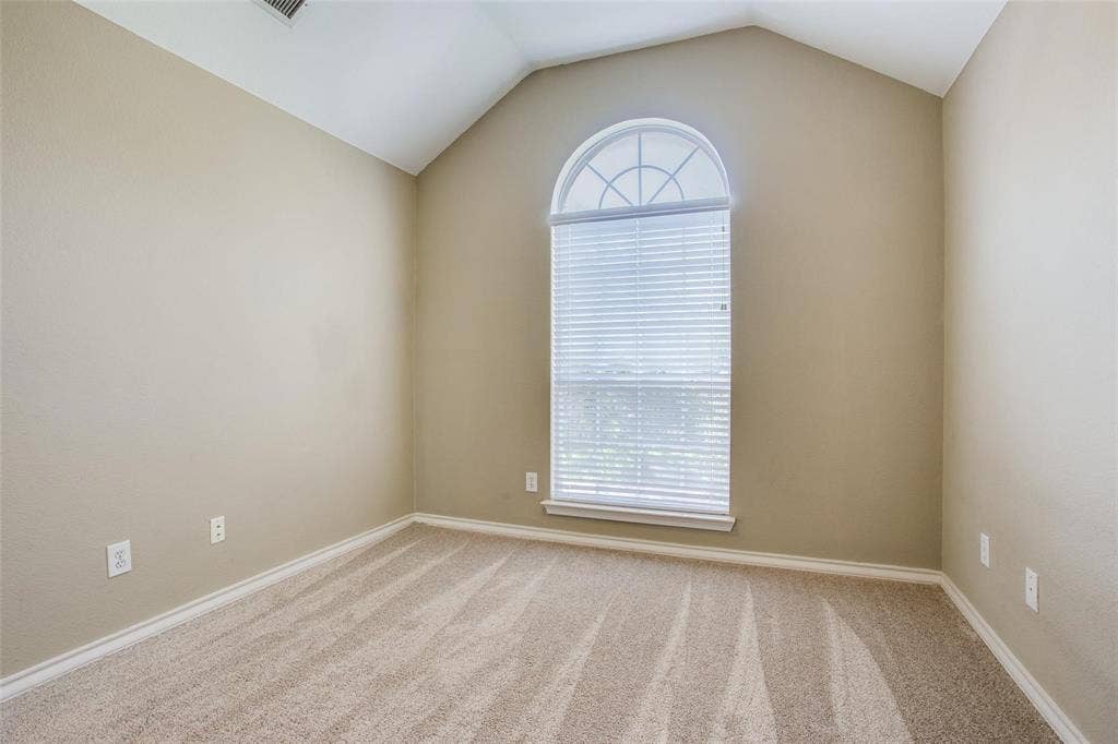 Room featuring a vaulted ceiling, neutral wall tones, carpeting, and a large window with an arched transom