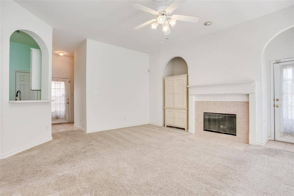 Living area featuring a fireplace with a masonry surround, arched architectural details, built-in cabinetry, and a ceiling fan