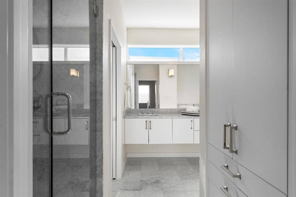 Floating vanity with stone countertop, glass-enclosed shower, built-in cabinetry, stone flooring, and clerestory windows