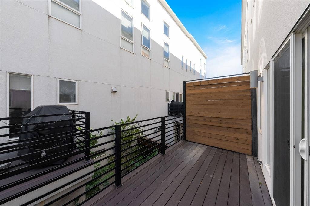 Exterior balcony featuring composite decking, horizontal metal railings, and a wood-slat privacy screen