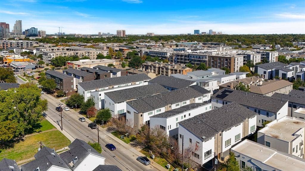 Aerial perspective featuring contemporary multi-story residences with pitched shingle roofing and minimalist exterior finishes, situated within an urban skyline setting