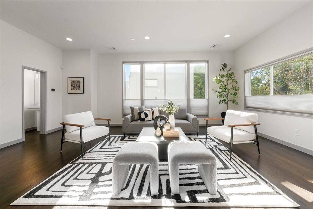 Living area featuring wood-finish flooring, recessed lighting, and large picture windows with horizontal shades