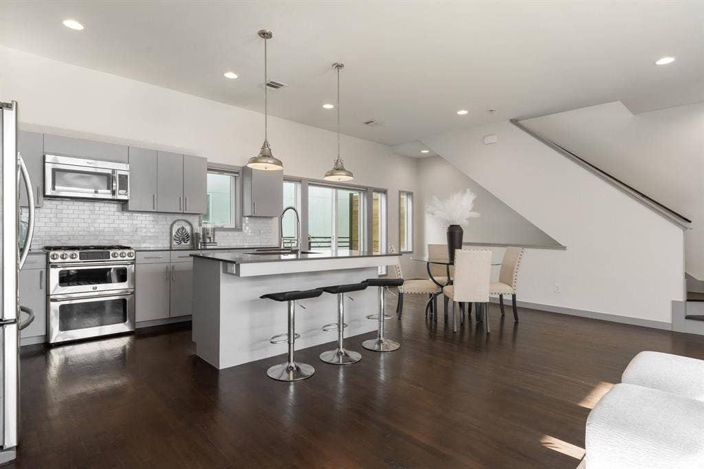 Modern kitchen featuring flat-panel cabinetry, stainless steel appliances, a tile backsplash, wood-finish flooring, and a center island with pendant lighting