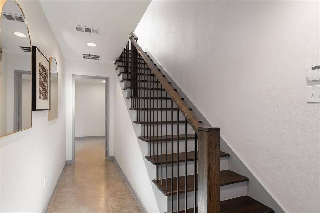 Staircase featuring wood treads, a dark wood handrail, and black metal balusters, complemented by smooth concrete-finish flooring and recessed lighting
