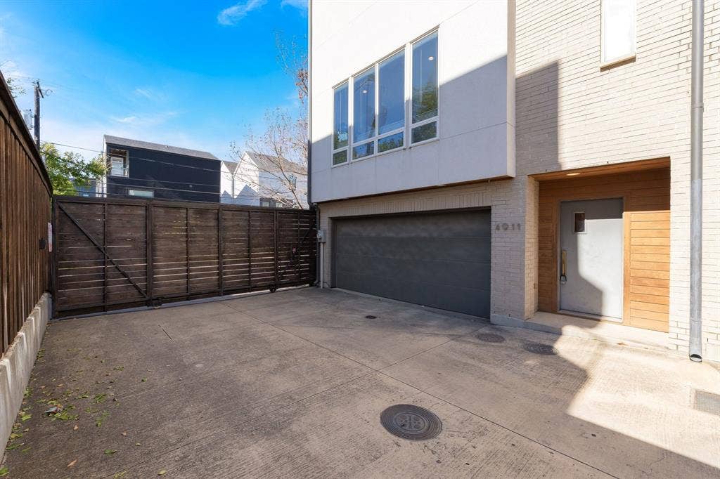 Modern exterior featuring a brick facade with horizontal wood siding accents, an integrated multi-car garage, large rectangular windows, and a privacy fence
