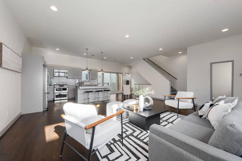 Open-concept living space featuring wood-finish flooring, recessed lighting, stainless steel appliances, a kitchen island with stone countertops, and a staircase with a dark metal railing