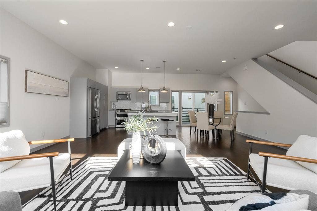 Open-concept living space featuring wood-finish flooring, recessed lighting, stainless steel kitchen appliances, a central island, and a staircase with a wooden handrail