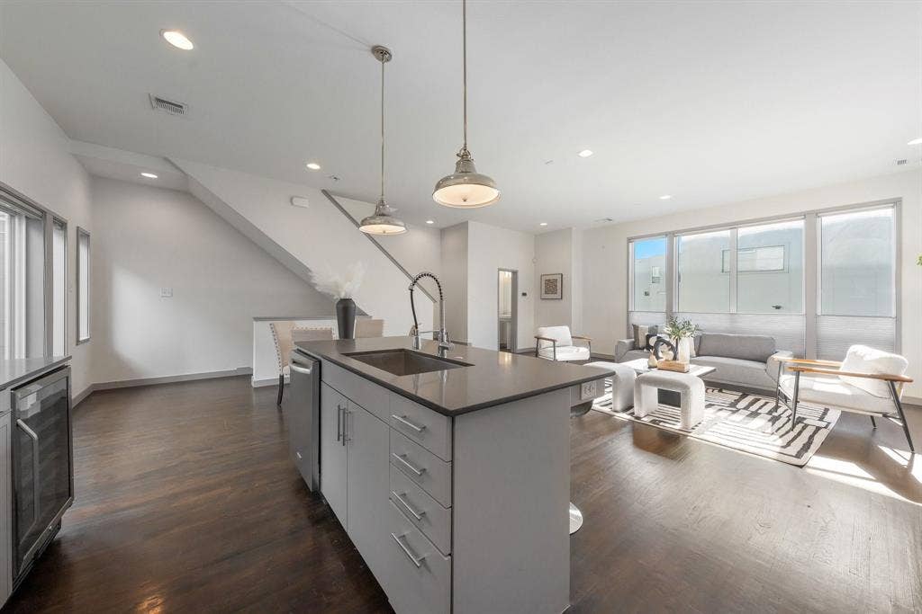 Open-concept kitchen featuring an island with a stone-composite countertop, stainless steel undermount sink, and high-arc faucet, complemented by wood-finish flooring and pendant lighting