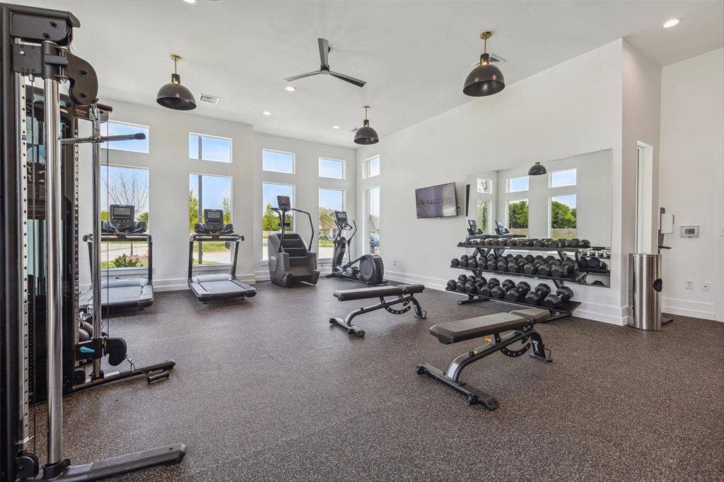 Fitness area with large wall-mounted mirror, multiple windows, ceiling fan, and recessed lighting