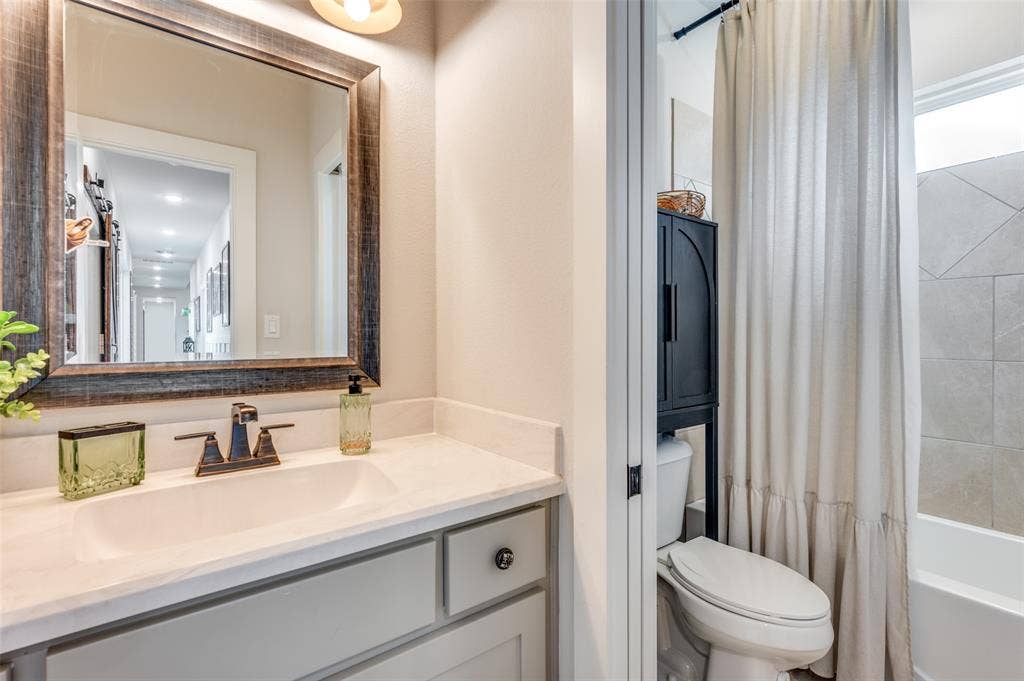 Bathroom featuring a vanity with a neutral-toned countertop, undermount sink, and oil-rubbed bronze faucet, paired with a framed mirror and a tile-surround tub
