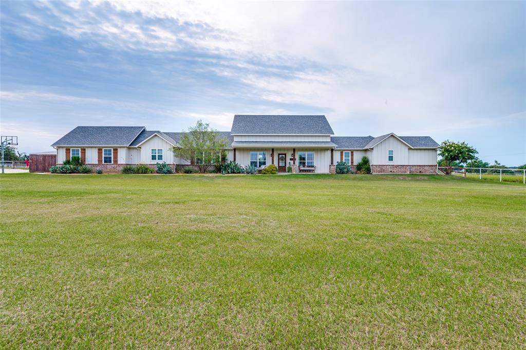 Single-story ranch exterior featuring board-and-batten siding, a brick facade, shingle roofing, and an expansive lawn