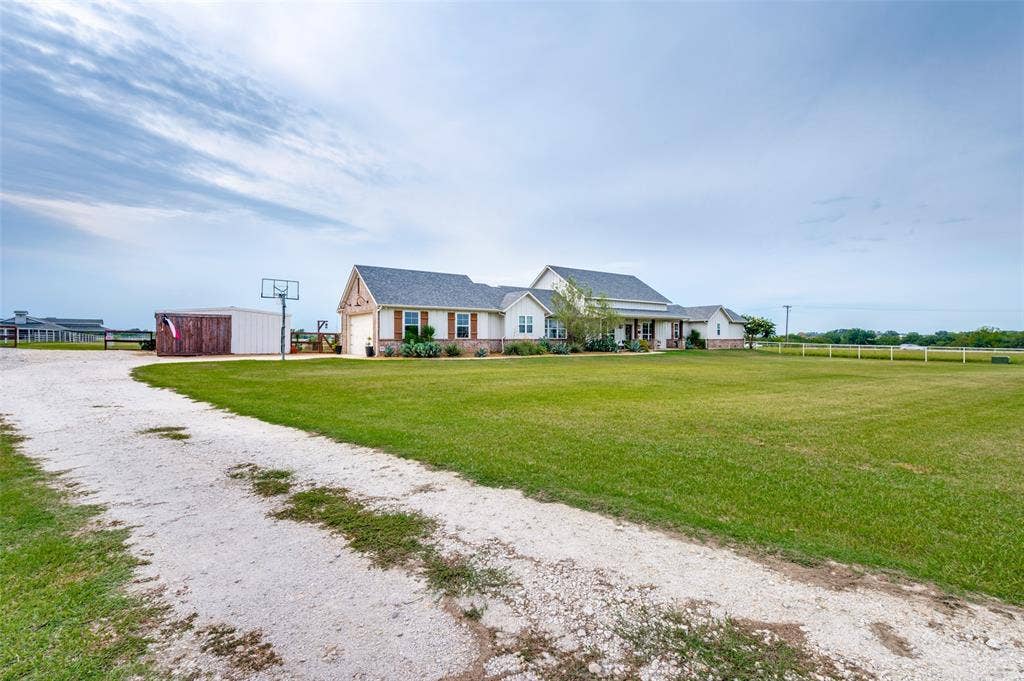 Exterior featuring a multi-gabled roofline, stone and siding facade, extensive grassy acreage, and a gravel driveway