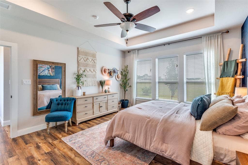 Tray ceiling featuring a dark-finish ceiling fan, wood-finish flooring, and expansive windows with horizontal blinds