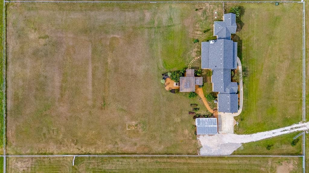 Aerial perspective of a sprawling fenced lot featuring a multi-gable residence, detached structure, stone-paver walkways, and a gravel driveway