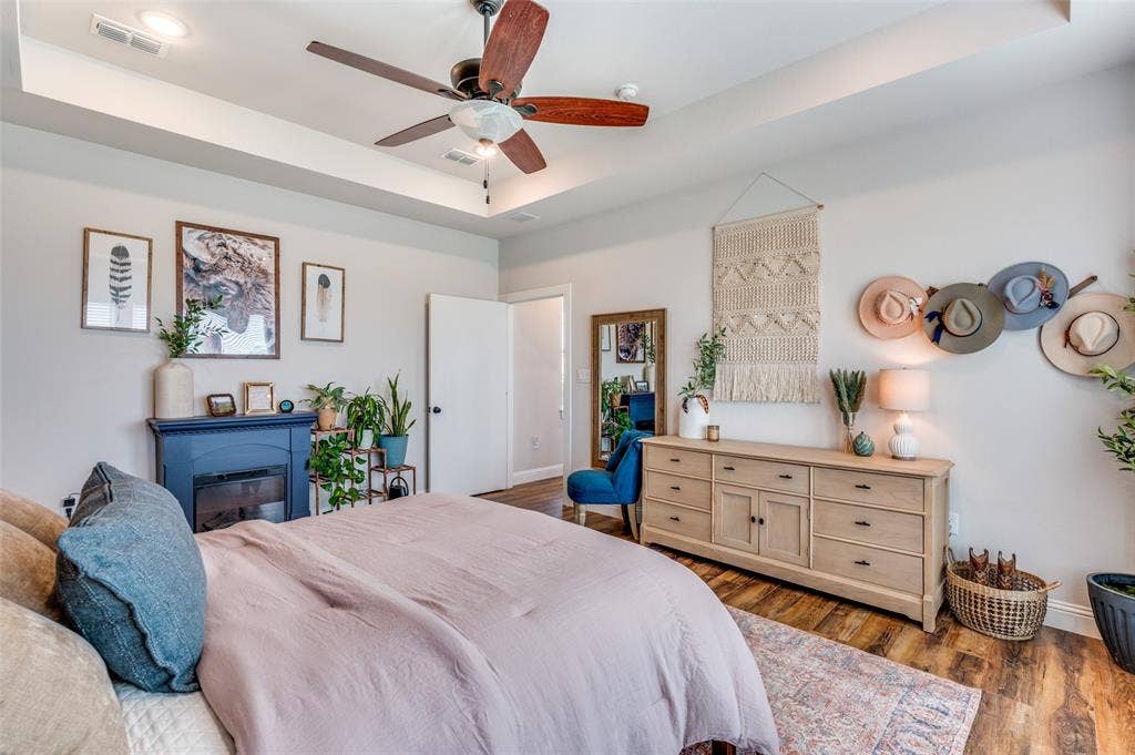 Tray ceiling, wood-finish flooring, ceiling fan with light fixture, and blue-painted built-in electric fireplace