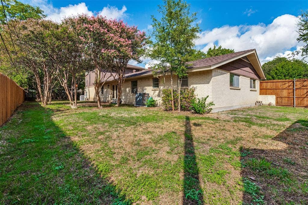 417 Keats Circle, Irving, TX 75061 Exterior featuring a brick and horizontal siding façade, expansive lawn, mature shade trees, and wood privacy fencing