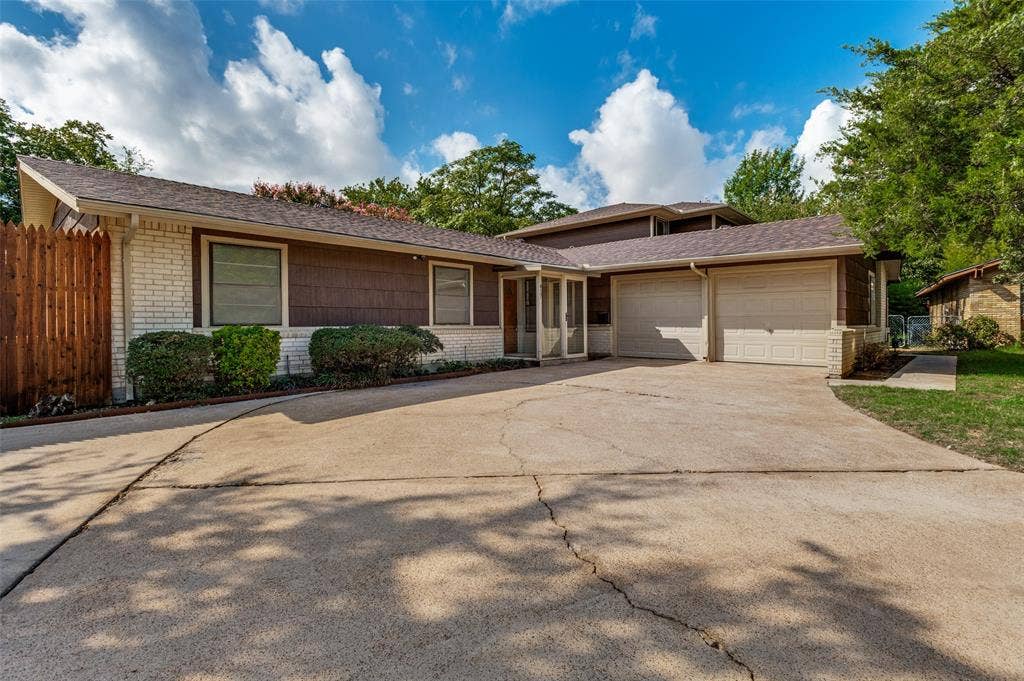 417 Keats Circle, Irving, TX 75061 Multi-level exterior featuring a combination of brick and wood-shingle siding, a two-car garage, and a wood privacy fence