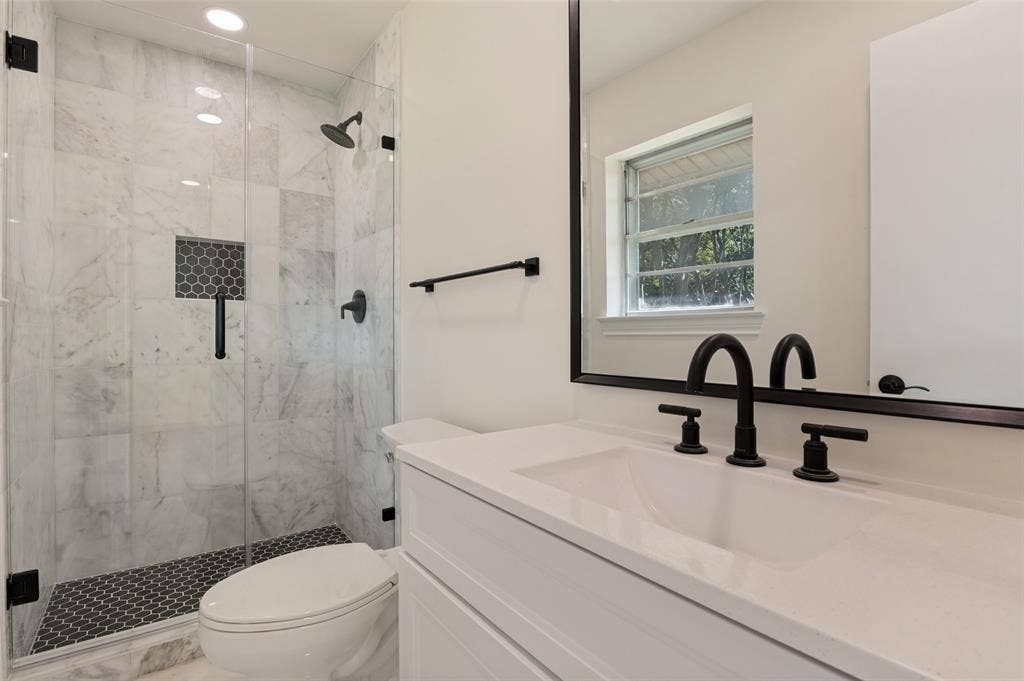 417 Keats Circle, Irving, TX 75061 Walk-in shower with stone-tile surround, glass enclosure, and black matte fixtures, paired with a white vanity featuring a quartz countertop and black-framed mirror