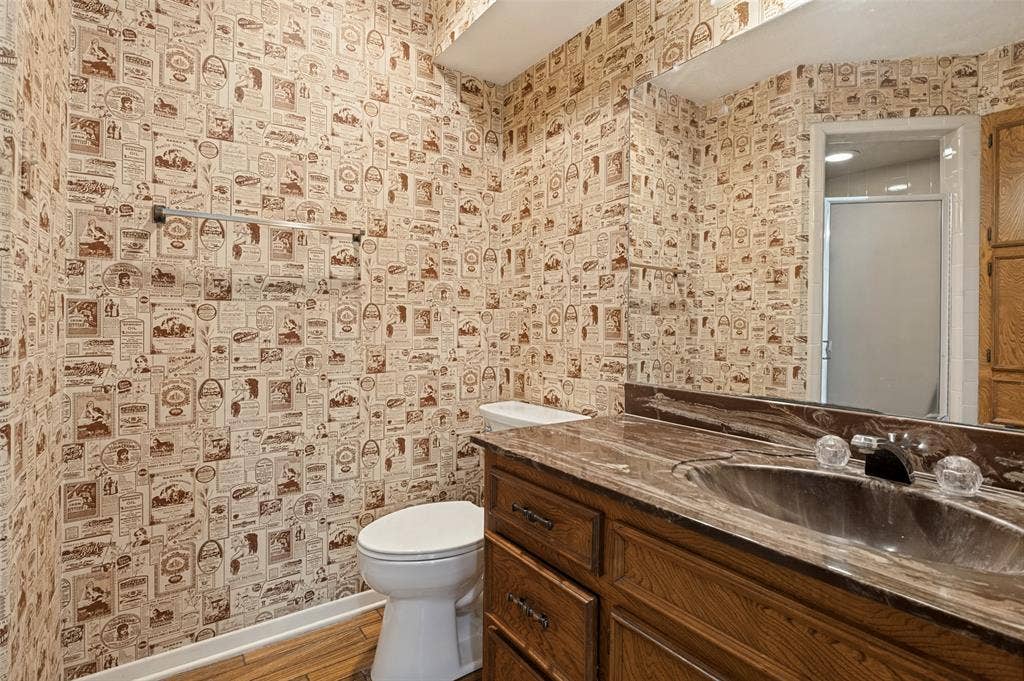 417 Keats Circle, Irving, TX 75061 Bathroom featuring a stone-finish countertop with an integrated basin, wood cabinetry with metallic hardware, a wall-spanning mirror, and a towel bar