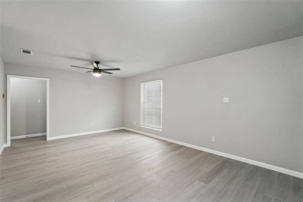 Spacious room featuring wood-finish flooring, neutral wall paint, and a ceiling-mounted light fixture with fan blades