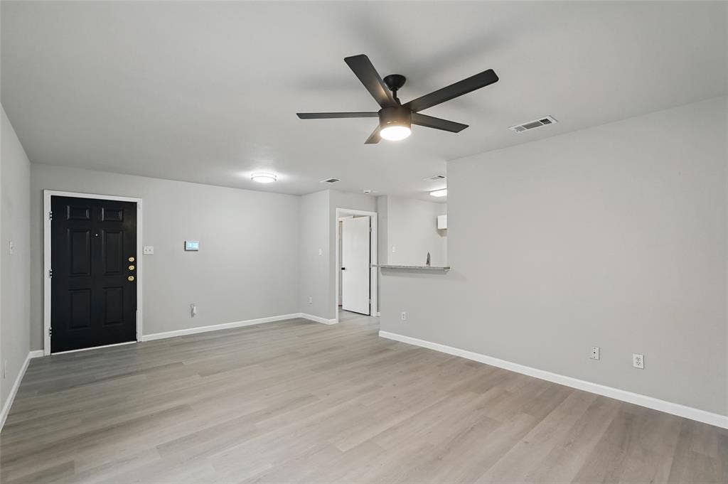 Interior space featuring wood-finish flooring, a matte black six-panel entry door, a multi-blade ceiling fan with integrated lighting, and a stone-surface breakfast bar