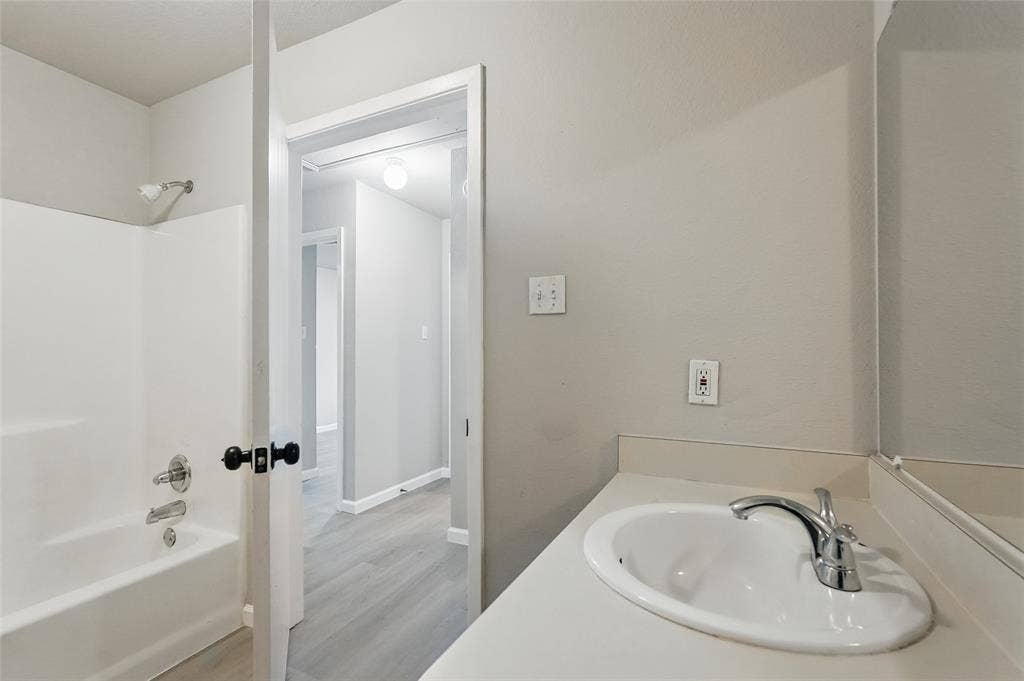 Bathroom featuring a tub-shower combination with integrated surround, vanity with an integrated basin, chrome-finish faucet, and wood-finish flooring