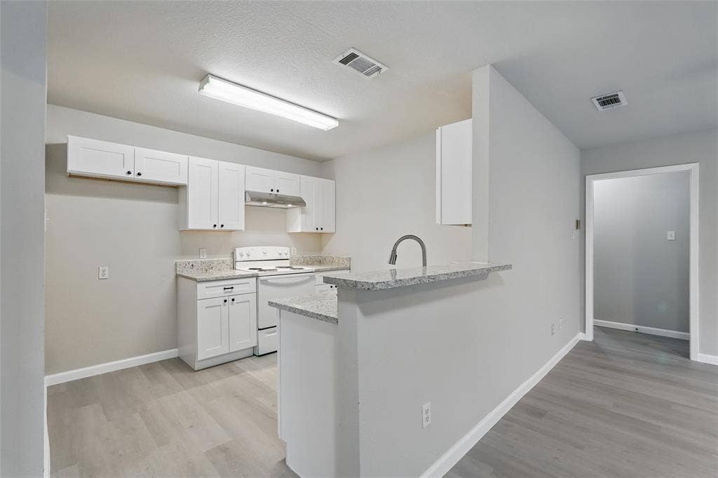 Kitchen featuring white cabinetry, stone-finish countertops, stainless steel range hood, peninsula with an integrated sink, and wood-finish flooring
