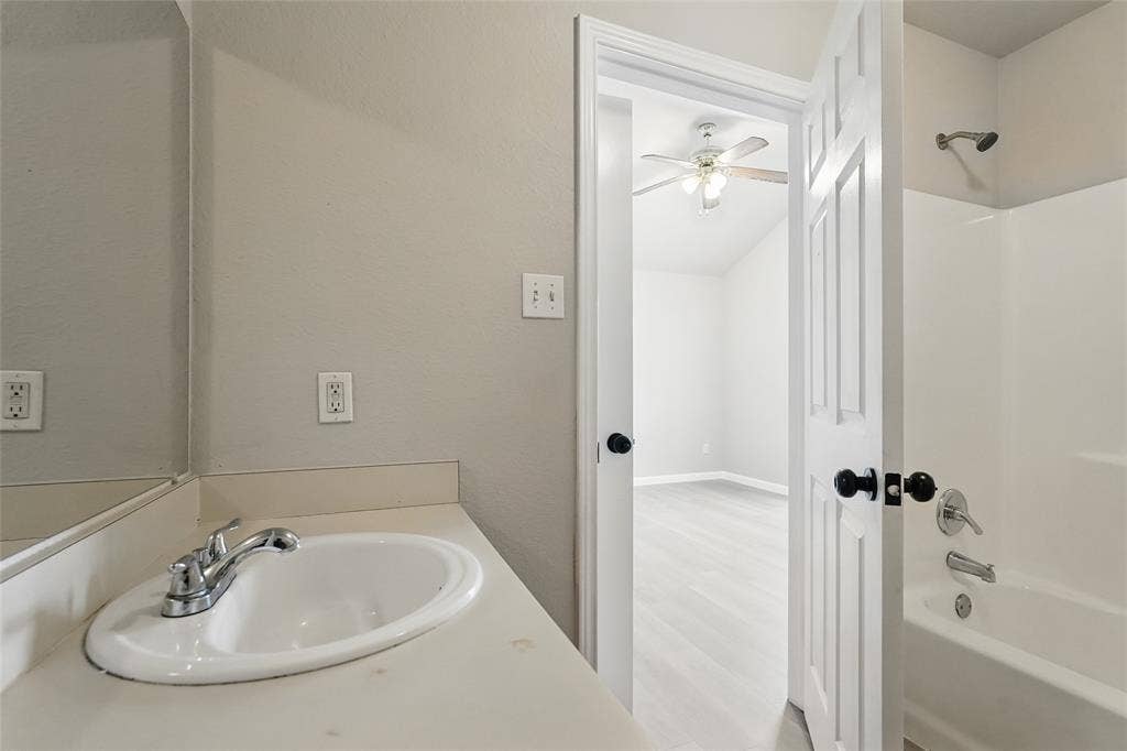 Bathroom featuring a vanity with a white integrated sink, a large wall-mounted mirror, a tub-shower combination, and a six-panel door with black hardware