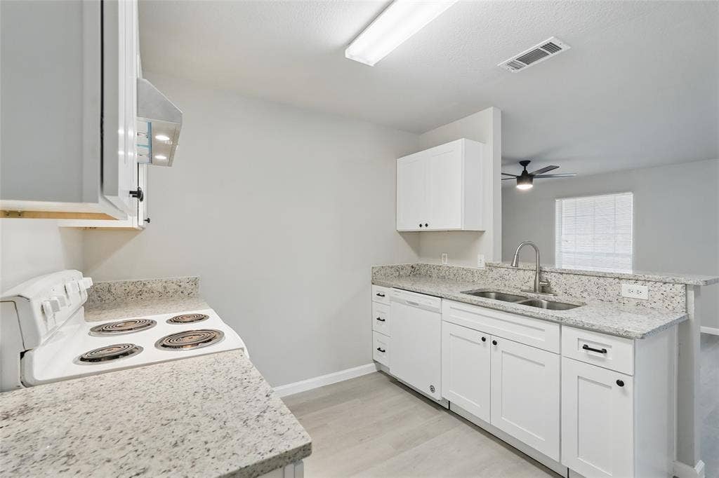 Kitchen featuring white shaker-style cabinetry, stone-finish countertops, stainless steel dual-basin sink with gooseneck faucet, integrated electric range, and wood-finish flooring