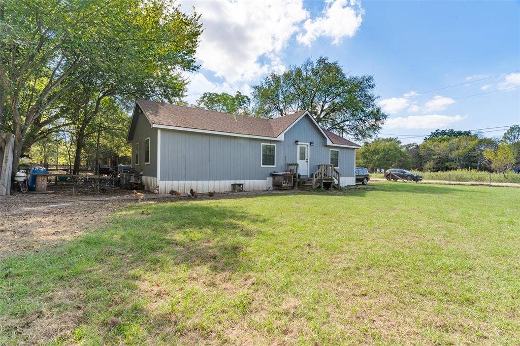 1219 Green Tree Acres Road, Kemp, TX 75143 Single-story residence featuring vertical siding, a composition shingle roof, white trim detailing, and an expansive lawn with mature shade trees