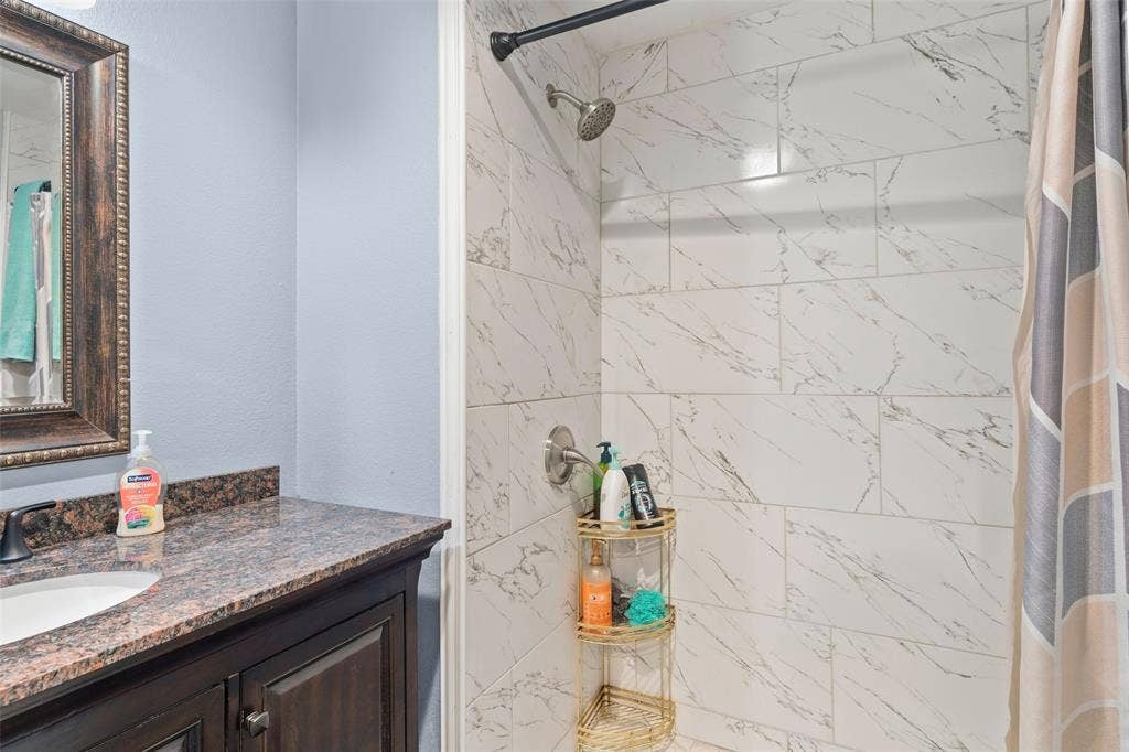 1219 Green Tree Acres Road, Kemp, TX 75143 Bathroom featuring a vanity with a stone countertop and an undermount sink, paired with a shower enclosure showcasing large-format, marble-patterned tile surrounds