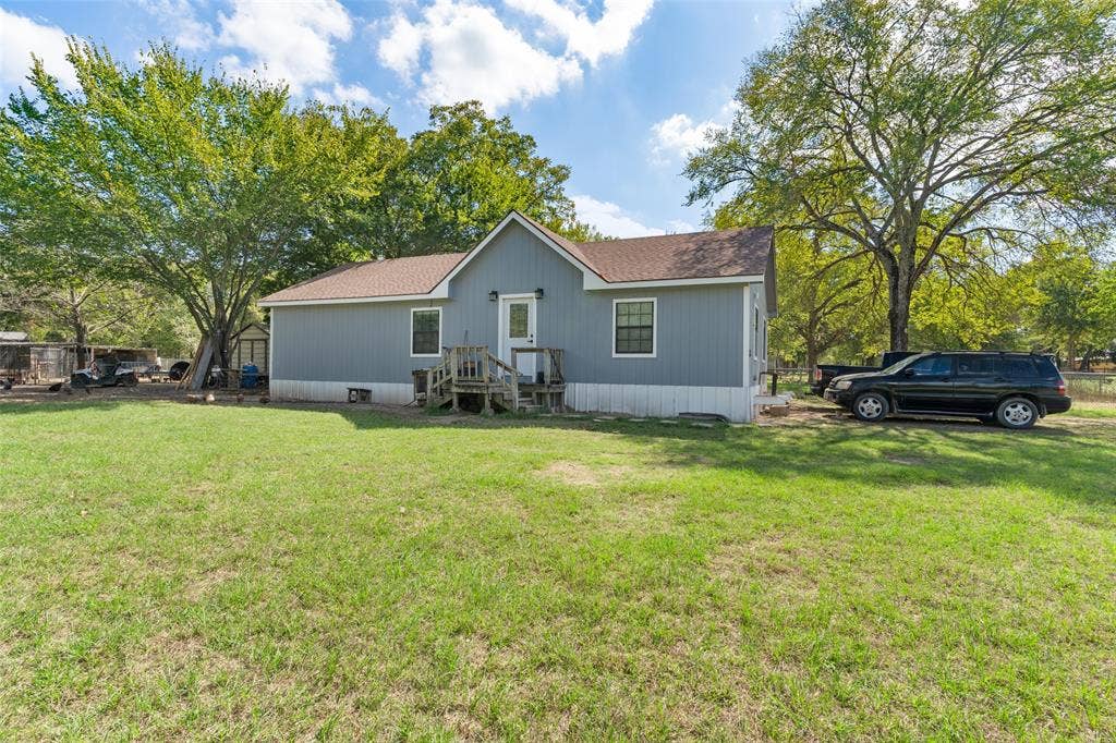 1219 Green Tree Acres Road, Kemp, TX 75143 Single-story residence featuring grey vertical siding, a shingle roof, white trim accents, and a wooden porch entry, set on a property with mature trees