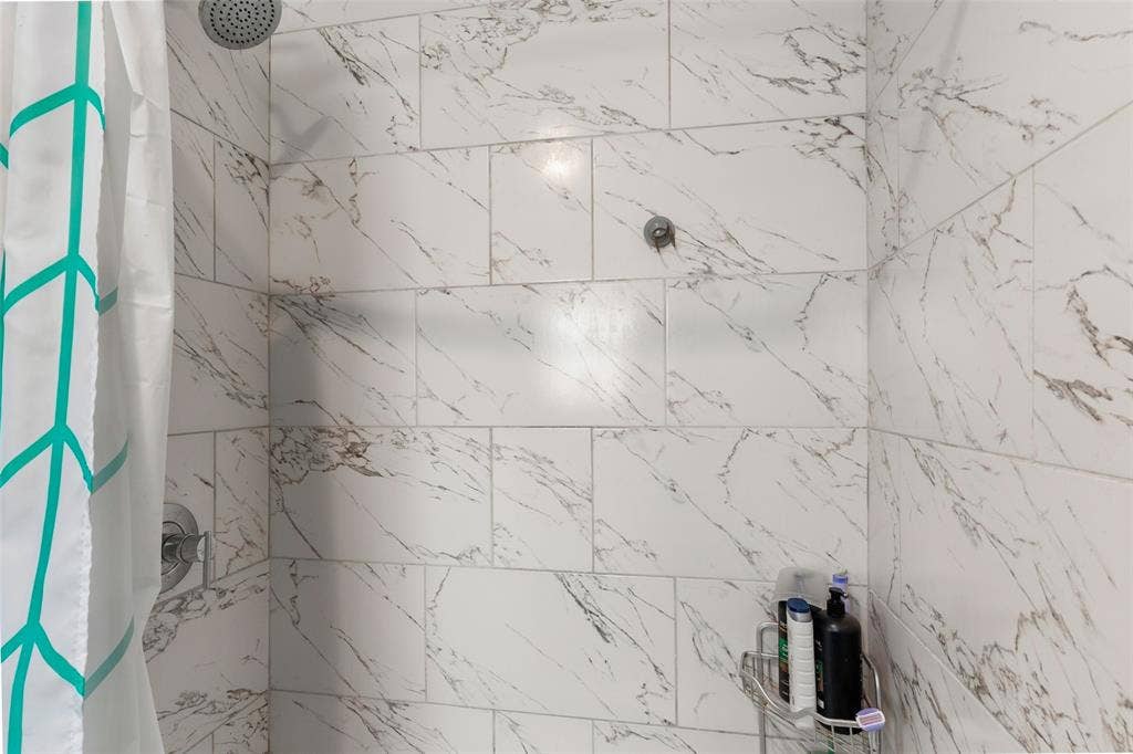 1219 Green Tree Acres Road, Kemp, TX 75143 Shower enclosure featuring large-format, light-toned stone-patterned wall tile, polished chrome shower head, and matching chrome pressure-balance valve