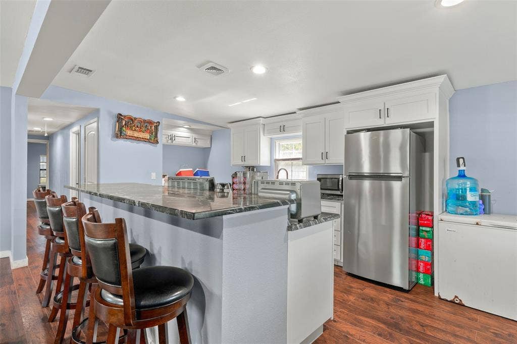 1219 Green Tree Acres Road, Kemp, TX 75143 Kitchen featuring a stone-surface breakfast bar, white cabinetry, wood-finish flooring, and stainless steel refrigerator