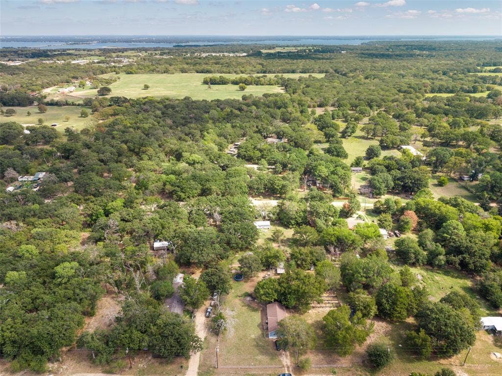 1219 Green Tree Acres Road, Kemp, TX 75143 Aerial perspective of a sprawling parcel featuring expansive tree coverage, cleared open space, and distant water scenery