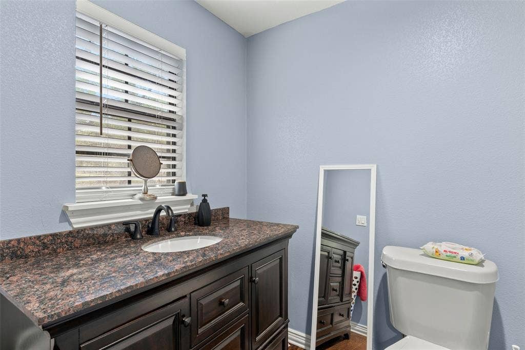 1219 Green Tree Acres Road, Kemp, TX 75143 Dark wood cabinetry featuring raised-panel doors, stone-finish countertop, undermount sink with matte black faucet, and horizontal slat window blinds