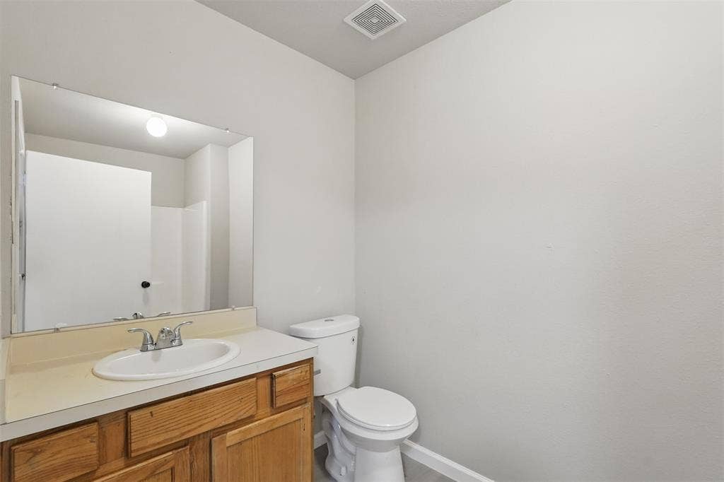 Bathroom featuring a wooden vanity, a drop-in sink with a dual-handle faucet, a flat-panel wall mirror, and a standard-height toilet