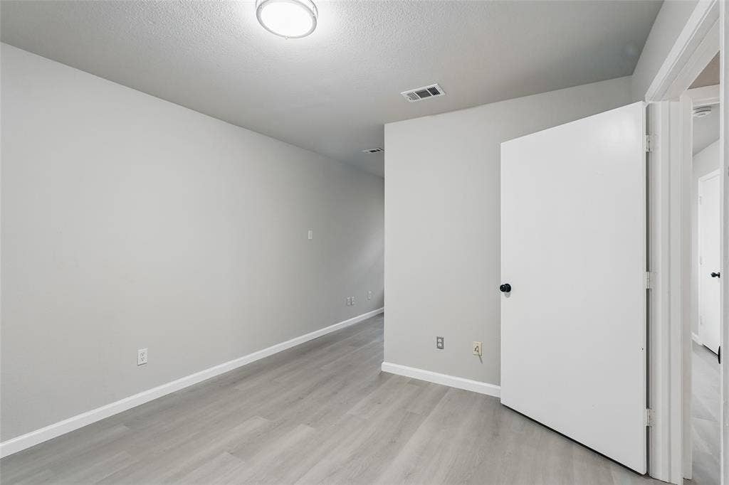 Neutral-toned room featuring wood-finish flooring, a white interior door, and a flush-mount overhead light fixture