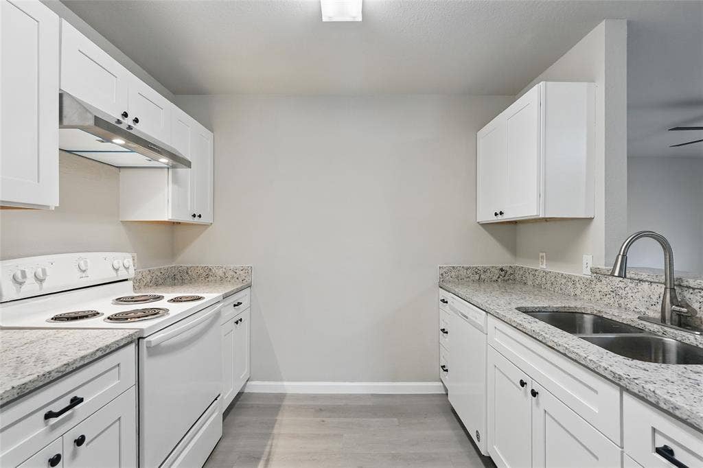 Kitchen featuring white shaker-style cabinetry, stone-finish countertops, stainless steel dual-basin sink with arched faucet, overhead range hood, and wood-finish flooring