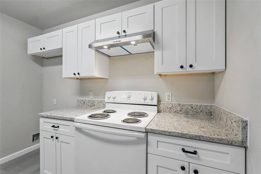 White shaker-style cabinetry, speckled stone-finish countertops, stainless steel range hood, and matte black hardware