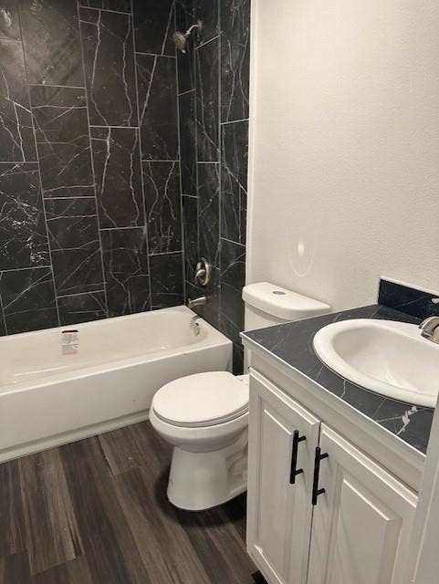 1613 Campbell Street, #A, Commerce, TX 75428 Bathroom featuring vertical dark stone-finish tile shower surround, white cabinetry, dark stone-finish countertop with integrated sink, and wood-finish flooring