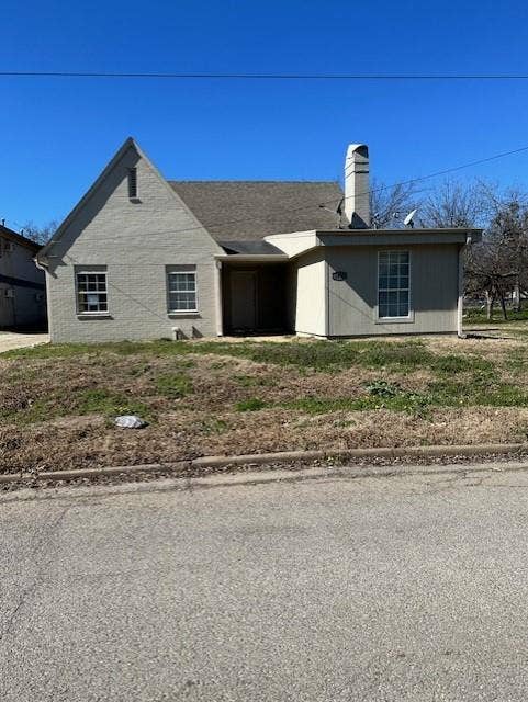 1613 Campbell Street, #A, Commerce, TX 75428 Exterior featuring a painted brick facade, steep gabled roofline, prominent exterior chimney, and recessed entryway